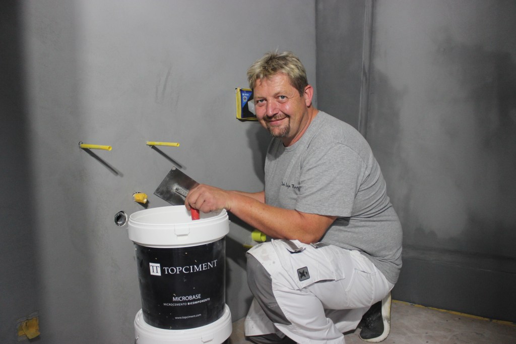Fachmann arbeitet mit Microzement von Topciment in einem Badezimmer, während er eine Wand vorbereitet.
