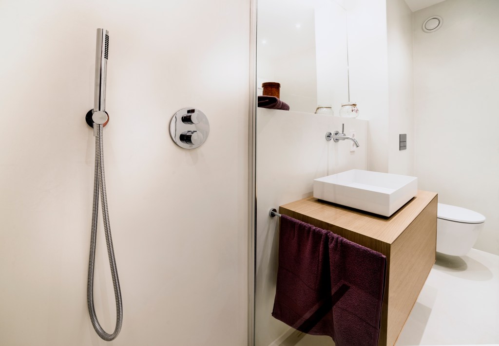 Modernes Badezimmer mit fugenloser Wandoberfläche, separater Dusche, Waschbecken auf Holzunterbau und WC.