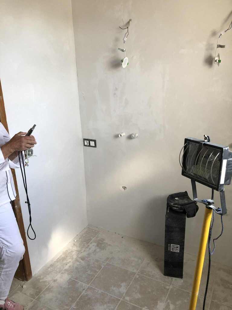 Innenraum mit unvollständiger Wandverkleidung, Werkzeug und Lichtquelle, das die Wichtigkeit der richtigen Vorbereitung für fugenlose Oberflächen zeigt.