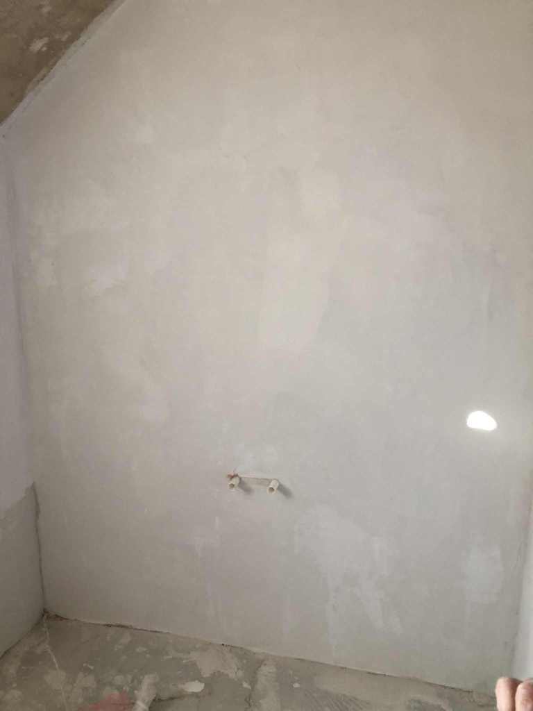 Unfertige Wandfläche mit glatter Oberfläche, bereit für die Endbearbeitung in einem Raum.