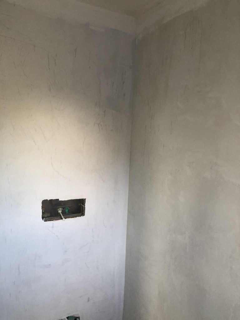 Unbearbeitete Wand mit Mikrozement, sichtbar sind unregelmäßige Oberflächen und ein unvollendeter Steckdosenausschnitt.