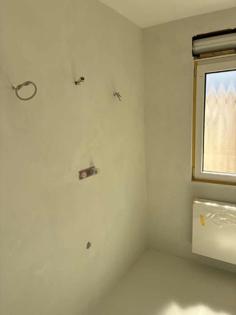 Ein unvollendeter Raum mit neu verputzten Wänden und sichtbaren Installationen, darunter Wasserhähne und Heizungsanschluss.