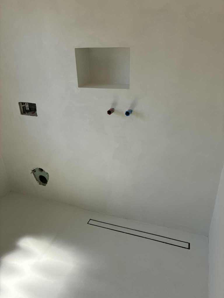 Unfertige Badezimmerwand mit Ausnehmungen für Armaturen und Ablauf.
