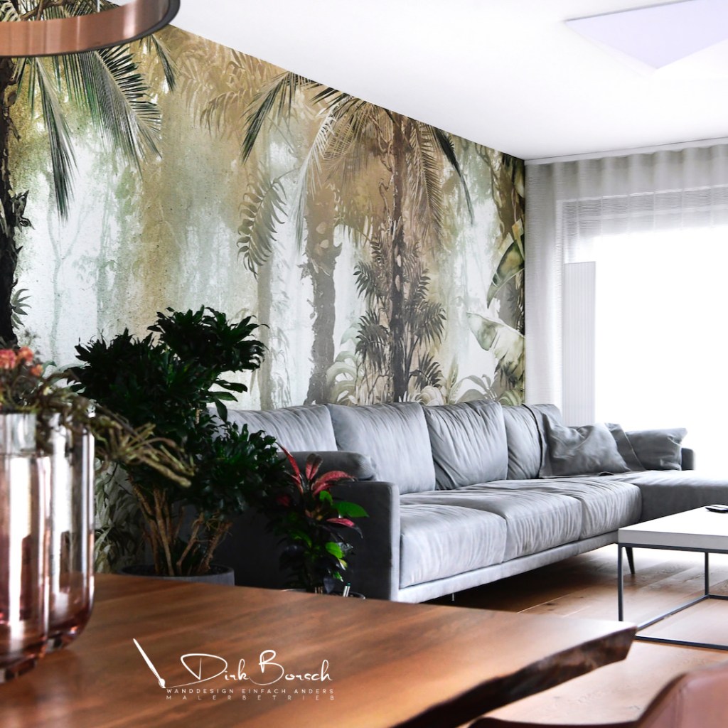 Heller Wohnbereich mit grauem Sofa, einem Holztisch und grünen Pflanzen, dekoriert mit einer tropischen Wandtapete.
